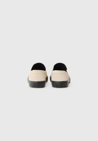 Beige plátěné nazouvací boty s černou gumovou podrážkou a nízkým střihovým zadním okrajem. Hladký povrch a minimalistický design bez viditelných detailů.
