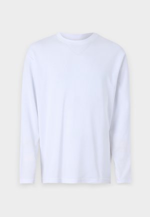 Valge pikkade varrukatega T-särk, mis on valmistatud pehmest puuvillast, omab ümarat kaelust ning diskreetseid õmbluse detaile ees ja õlgadel.