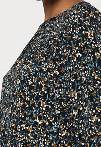 Kukkakuosiset mekko mustalla taustalla, jossa on valkoisia, ruskeita ja vaaleansinisiä kukkia. Pehmeä kangas rentoa istuvuutta. Pyöreä pääntie.