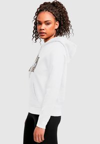 Vit sweatshirt med ficka fram, dragsko på huvan och grafisk tryck. Mjukt tyg, figurnära design, långa ärmar och ribbade muddar.