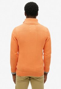 Pomarańczowy sweter z dzianiny z wysokim kołnierzem, prążkowanymi mankietami i dołem. Gładka struktura, dopasowany fason oraz średniej wagi materiał.