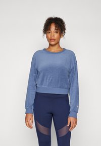 Blauer, weicher Sweatshirt mit lockerer Passform, Rundhalsausschnitt und langen Ärmeln. Kombiniert mit dunkelblauen Leggings mit transparenten Einsätzen.
