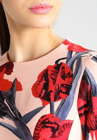 Blomstret kjole med en lyserød baggrund, prydet med store røde blomster og grønne blade. Glat materiale med rund halsudskæring og korte ærmer.