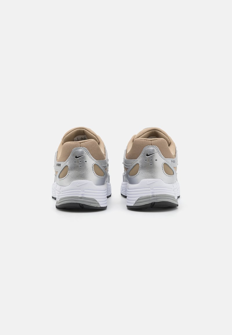Sneakers Nike w kolorze srebrnym, beżowym i białym. Okrągły kształt, wierzch z siateczki, amortyzowana podeszwa, wyraźne logo i odblaskowe akcenty.