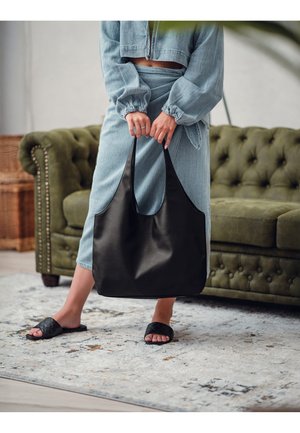 Černá kožená taška přes rameno s širokými popruhy, hladkým povrchem a prostorným tělem. Nositá s džínovým outfitem a sandály.