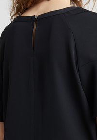 Czarna odzież z zamknięciem na plecach w kształcie dziurki do klucza z guzikiem, gładka struktura materiału i szerokie rękawy. Minimalistyczny design i czyste linie.