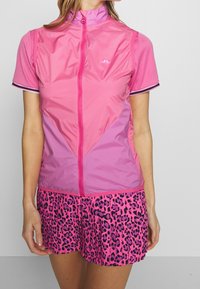 Růžový dvoudílný outfit s lehkou, zipovanou bundou s krátkým rukávem a barevnými bloky, doplněný o sukni šortky s leopardským potiskem.