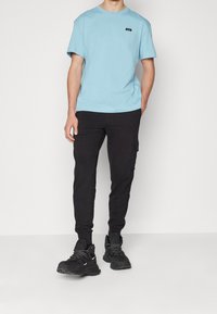 Ljusblå bomull t-shirt med rund halsringning, kombinerad med svarta, avsmalnande cargobyxor med sidfickor och svarta sneakers.