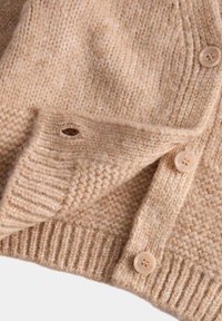 Světle béžový pletený cardigan s ribbovaným lemem a manžetami, čtyřmi plastovými knoflíky a malým detailem v podobě dírky. Měkká, texturovaná tkanina.