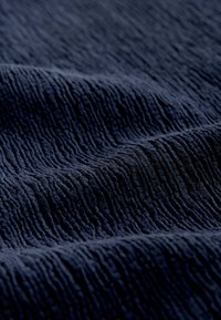 Temno modra kordurova tkanina z bližnjim posnetkom, ki prikazuje mehke, izbočene navpične grebene in nežne gube, ki ustvarjajo teksturirano površino.