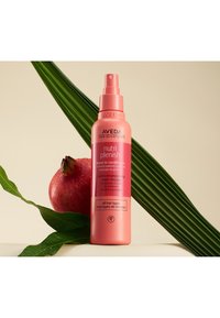 Flacon de conditionneur sans rinçage Aveda en plastique rose. Équipé d'un vaporisateur, étiquettes en anglais et en français, sur un fond de feuillage vert et d'une grenade.