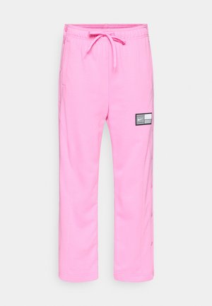 Lyserøde Nike træningsbukser med elastisk talje, snor, sidelommer, trykknapper langs benene og et sort-hvidt logo-patch på låret.