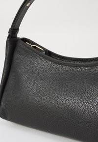 Černá kožená kabelka s texturovaným povrchem, zakřiveným tvarem a tenkým ramenním popruhem. Disponuje zlatým zapínáním.