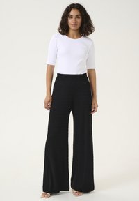Haut blanc à rayures, à manches trois quarts, associé à un pantalon noir à jambe large avec un tissage texturé et une coupe décontractée.