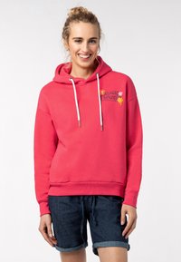 Roze hoodie met een vooraanstaande graphic met de tekst "Magic Flower", voorzien van een trekkoord in de capuchon en manchet-mouwen, gecombineerd met donkere denim shorts.