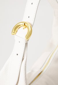 Sangle de sac en cuir blanc avec une finition texturée, dotée d'une boucle en métal doré et de trous réglables pour personnaliser la taille.