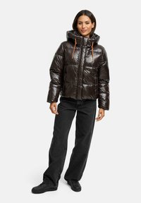 Puffig svart jacka med en blank yta, huva och orange draremmar. Kombinerad med svarta vida jeans och svarta sneakers.