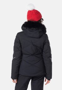 Svart isolerad jacka med diamantquiltat mönster och avtagbar huva med pälsfoder, tillsammans med en röd stickad mössa med en vit pompon.