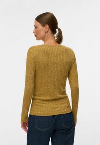 Kollase ribaga pika varrukaga särk, millel on ümar kaelus ja keha lähendav disain. Tekstuurne kangas peene mustriga, kombineeritud tumedate teksadega.