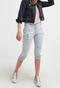 Ljust blå korta byxor med dragkedjefickor och knapppdetaljer, tillsammans med en randig skjorta och en mörk denimjacka. Silverfärgade sneakers.