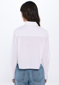 Camicia bianca a maniche lunghe con colletto, caratterizzata da una delicata texture, design cropped e orlo dritto. Abbina a jeans blu a vita alta.