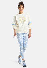 Cream sweatshirt with "90 ROXY" logo, blue and yellow stripes on sleeves; blue patterned leggings; light blue sneakers.