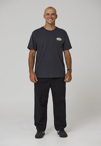 Mustast puuvillast t-särk, millel vasakul rinnal värvikas logo, kombineeritud lahtiste mustade pükstega ja mustade tossudega.