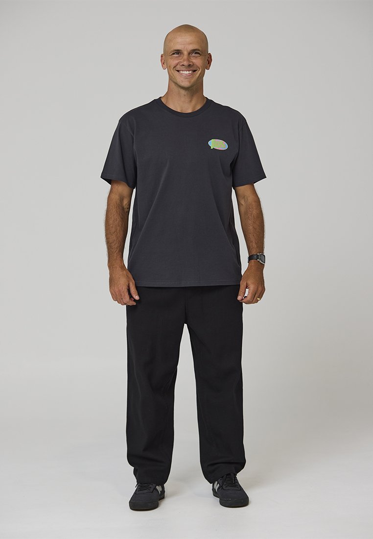 Mustast puuvillast t-särk, millel vasakul rinnal värvikas logo, kombineeritud lahtiste mustade pükstega ja mustade tossudega.