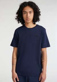 Camiseta de algod�ón azul marino con mangas cortas, escote redondo, que presenta un sutil logo negro en el pecho y una textura suave.