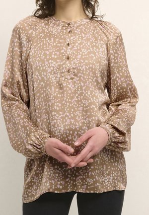 Brown blouse with a dotted pattern in pink and white. Features a round neckline, button closures, and gathered sleeve cuffs. Smooth texture.
