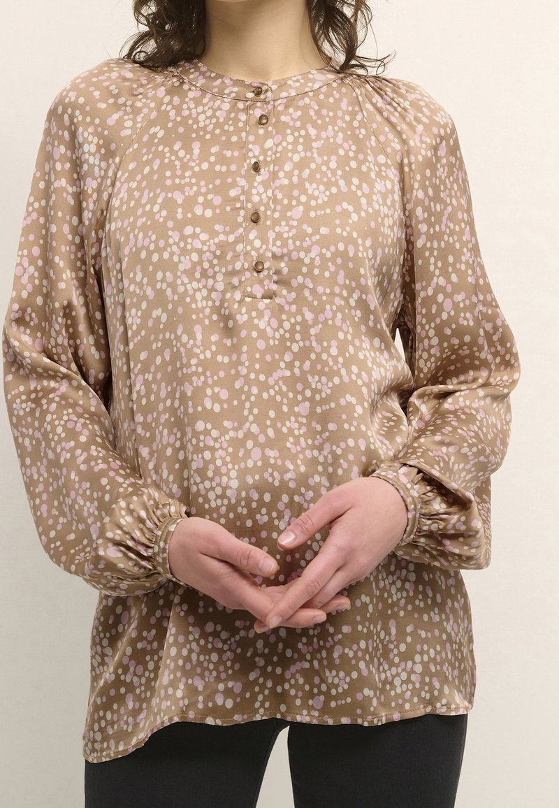 Brun blus med prickmönster i rosa och vitt. Har rund halsringning, knappstängning och smockade ärmslut. Mjuk textur.