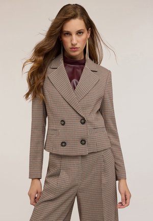 Blazer double boutonné à carreaux marron avec des revers accentués, des boutons noirs et des poches, associé à un pantalon assorti. Texture de tissu lisse.