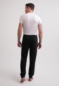 Witte fitted t-shirt gecombineerd met zwarte, loszittende, gestructureerde broek. De broek heeft een tailleband met trekkoord en zijzakken.