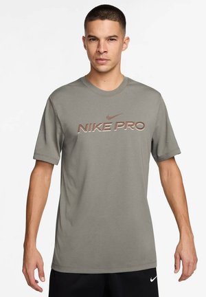 T-shirt Nike Pro in verde salvia, maniche corte, colletto rotondo, con il carattere audace "NIKE PRO" in un colore a contrasto. Tessuto dalla superficie liscia.