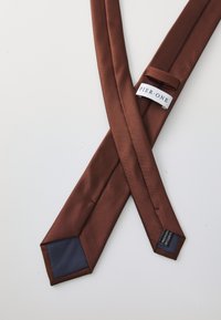 Cravate en satin marron avec des bords nets et un accent bleu marine à l'extrémité large. Présente une étiquette avec "PIER ONE" et une étiquette d'entretien de l'autre côté.