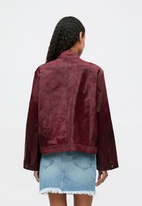 Veste en suède bourgogne avec une coupe décontractée, des manches larges et un ourlet droit, associée à une mini-jupe en denim bleu clair avec des bords effilochés.
