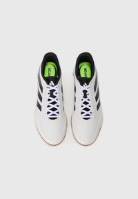 Para białych trampek Adidas Predator z czarnymi paskami, białymi sznurówkami i jaskrawozielonymi wkładkami na jednolitym białym tle.