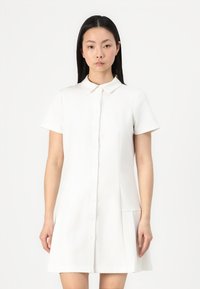 Rochie albă cu mâneci scurte, cu închidere prin butoni, guler și pliu lateral. Fabricată dintr-un material neted și ușor, cu un design minimalist.