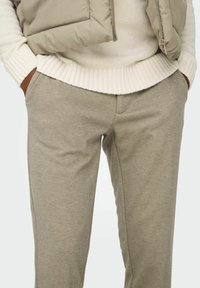 Pantaloni della tuta beige realizzati in tessuto morbido, con una superficie liscia e un taglio standard dotato di tasche discrete. Abbinati a un maglione crema.