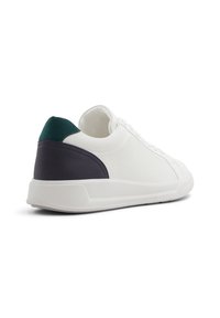 Sneaker bianco con una tomaia in canvas dalla texture, caratterizzata da accenti blu scuro e verde sul tallone e sul lato. Suola in gomma leggera.