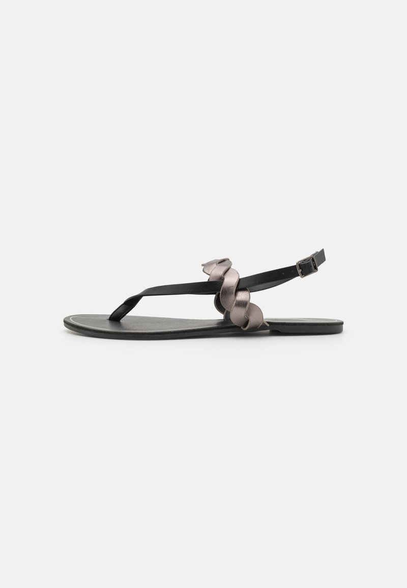 Svarta platta sandaler med en tunn rem och en dekorativ metallisk grå accent. Minimalistisk design, slät yta och justerbar ankelsläpp.