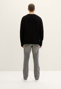 Suéter negro de punto con cuello redondo, combinado con jeans gris claro. Los jeans tienen detalles en los bolsillos traseros y un corte recto.