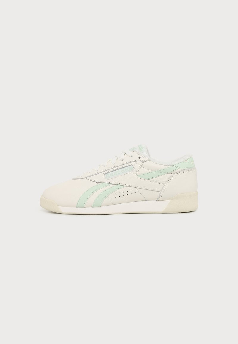 Baskets basses Reebok blanches et vert clair avec lacets à l'avant et détail perforé sur le côté sur un fond uni.