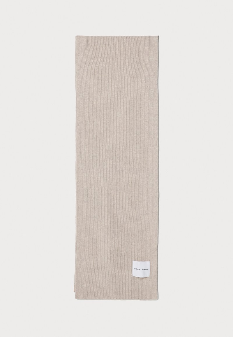 Beige ribbestrikket skjerf laget av et mykt strikket materiale. Har en liten vevd etikett i den ene kanten. Lang rektangulær form.