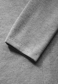 Grått stickat tyg med ett texturerat mönster; ärmsluten har en slät, ribbad mudd som förbättrar den övergripande designen och hållbarheten.