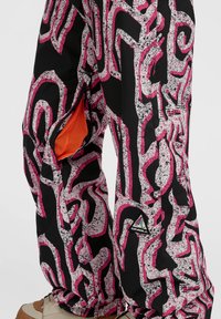 Zwarte broek met een abstract patroon in roze en wit; heeft een gaaszakopening en een logo-patch op het onderbeen.