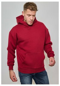 Hoodie rouge en tissu doux, avec une poche frontale, des poignets et un ourlet côtelés. Le design comprend une capuche spacieuse et une coupe décontractée.