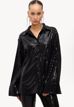 Camisa negra con lentejuelas, cuello con solapa, mangas largas y cierre de botones; presenta una superficie brillante y texturizada que refleja la luz.