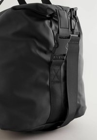 Black waterproof bag featuring a textured matte finish, adjustable nylon strap, and a plastic buckle closure, with subtle stitching details.