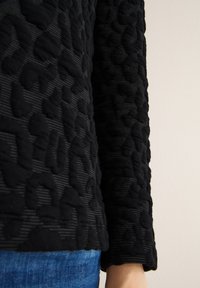 Černý svetr s texturou, kombinující vystouplé vzory a pruhy, s přiléhavým rukávem a měkkou skladbou látky.